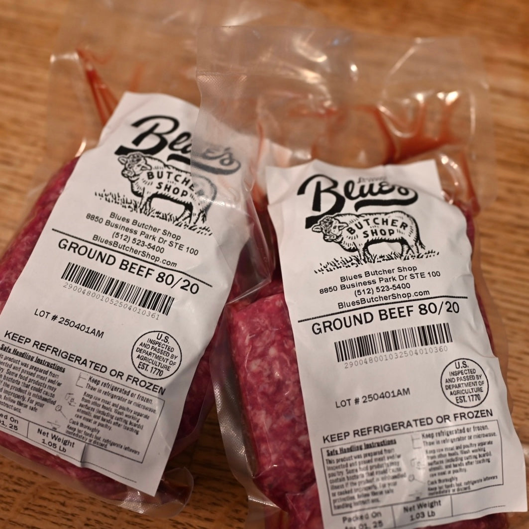 Two packages of ground beef with Blues Butcher Shop labels on a wooden surface.