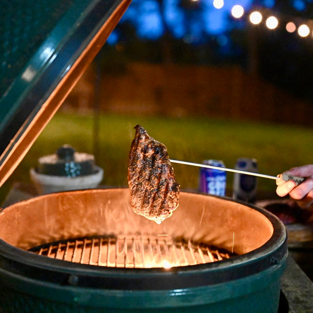 Grilled beef being lifted from a barbecue grill with a blurred outdoor background