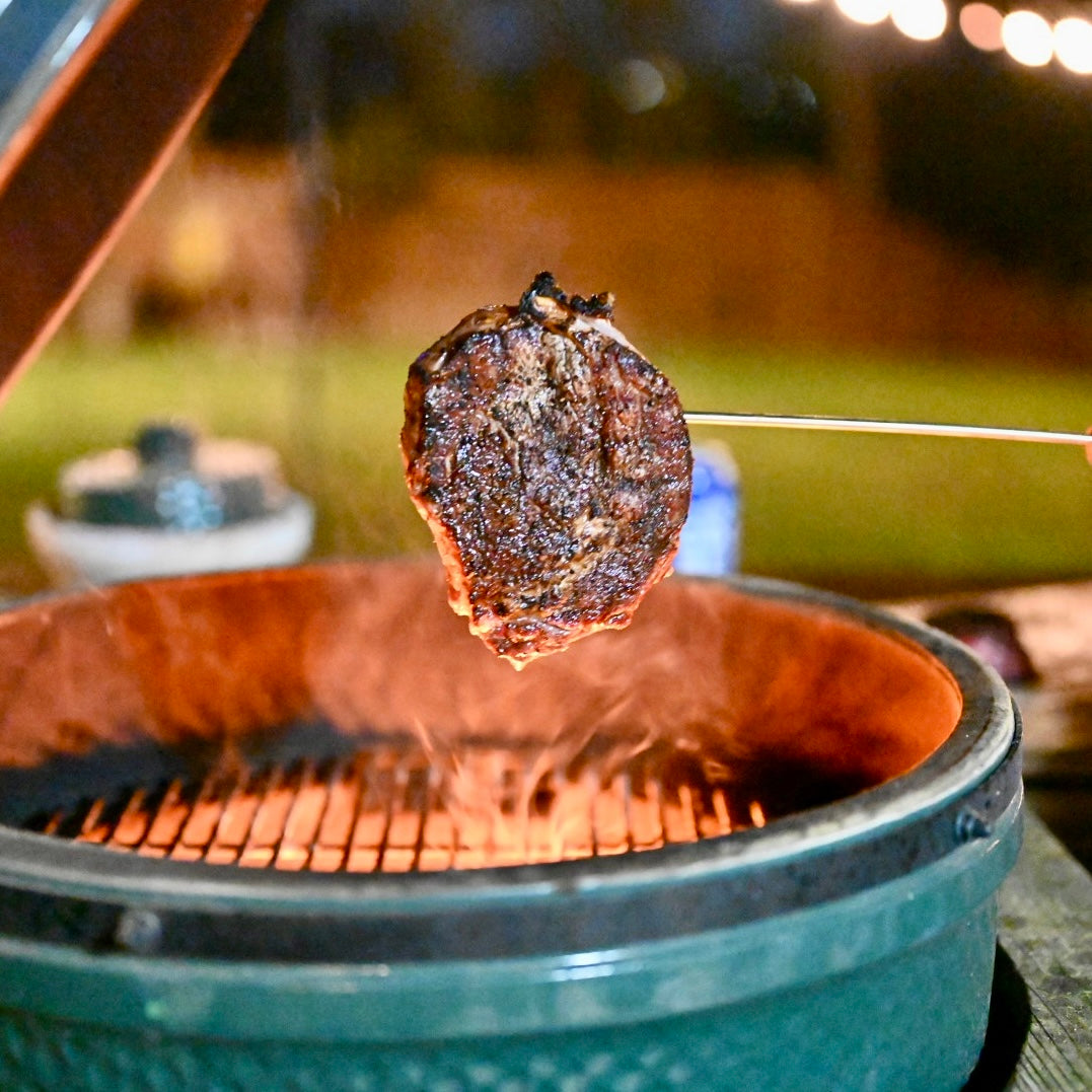 Steak being cooked on a grill with a blurred outdoor background