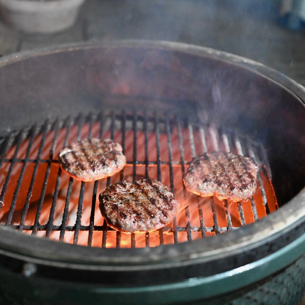 Three burgers cooking on a grill with flames