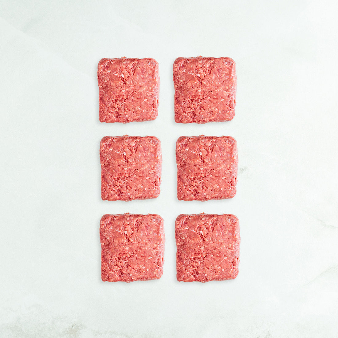 Six square pieces of ground meat on a white marble surface