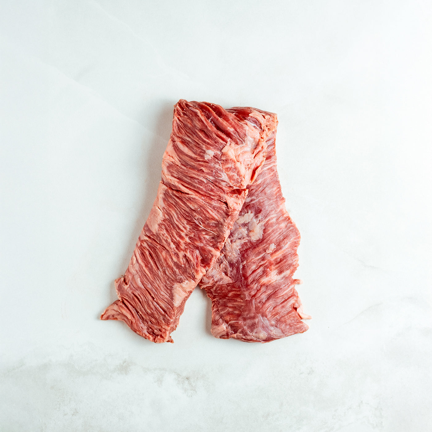 Raw outside skirt steak on a white marble surface