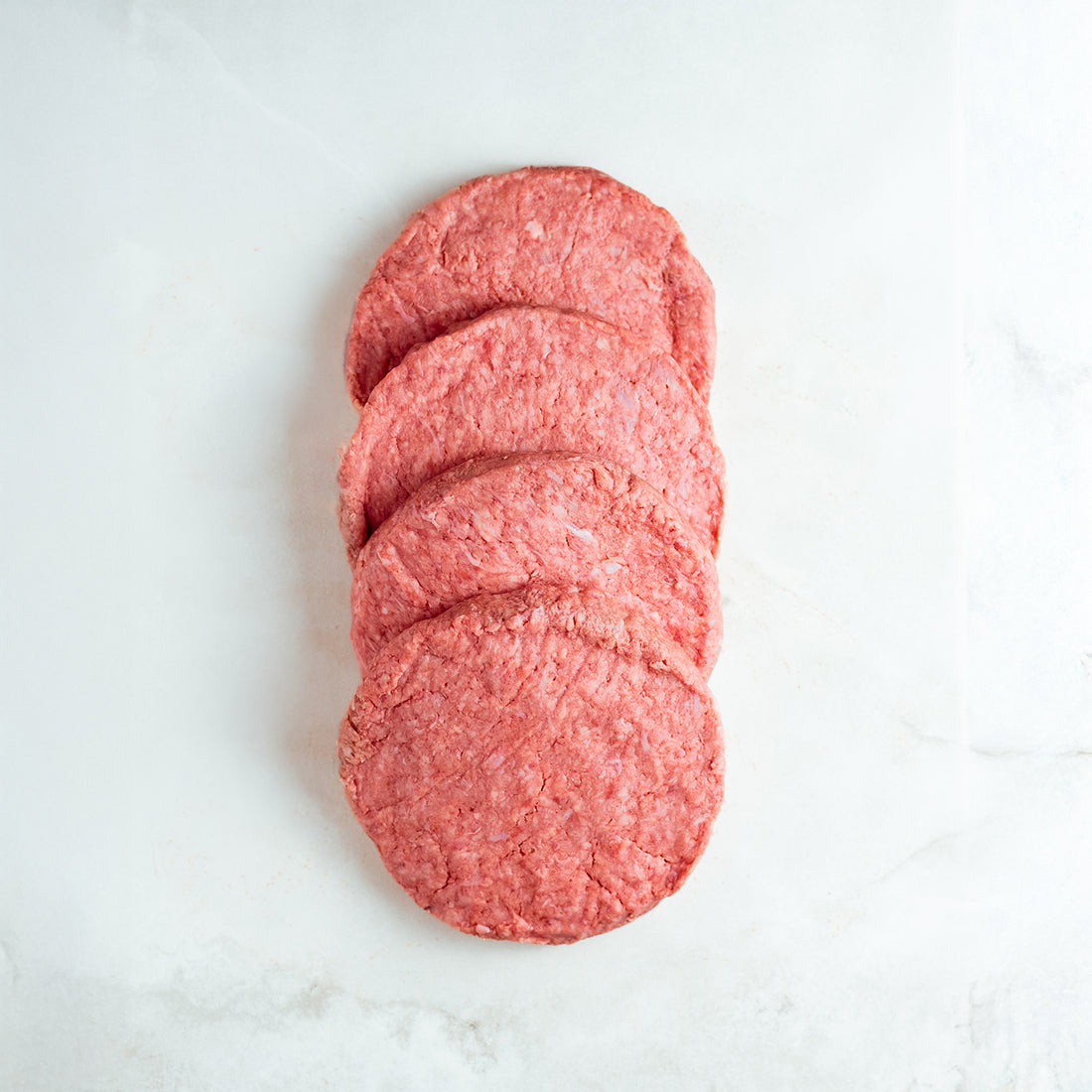 Stack of ground beef patties on a white marble surface