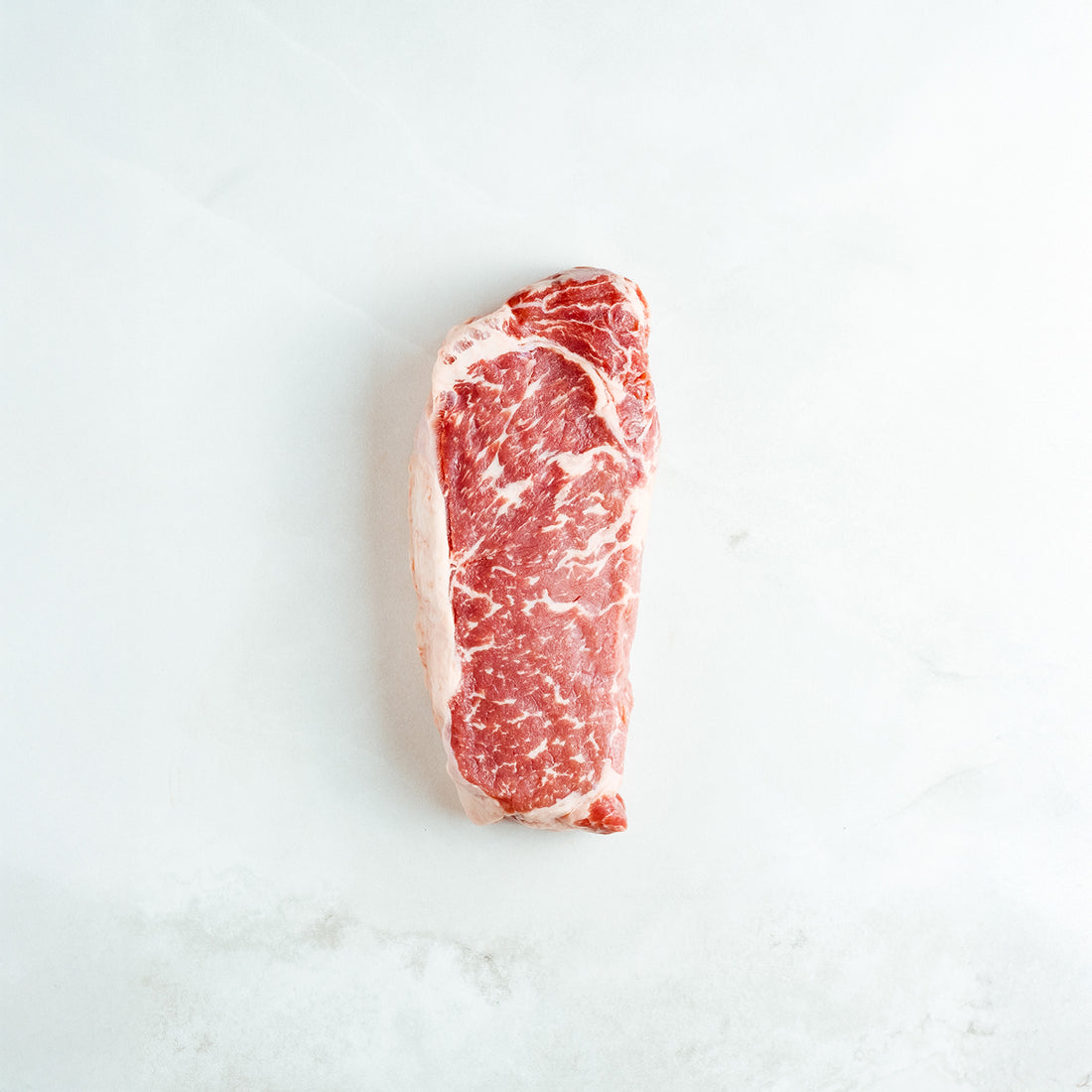 Raw texas strip steak on a white marble surface